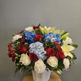 Mixed bouquet of red roses, blue hydrangeas, white carnations, and pale lilies in a white vase
