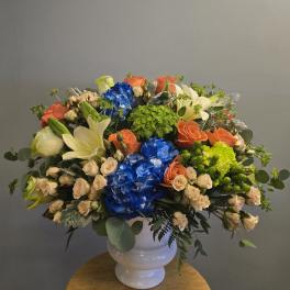 Large mixed bouquet in a white vase with blue, orange, cream, and green blooms
