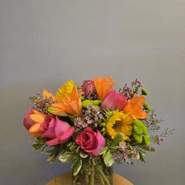 Bright mixed bouquet of roses, lilies, and sunflowers in a glass vase