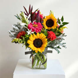 Mixed bouquet with sunflowers, pink blooms, and white flowers in a glass vase