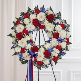 Red, white, and blue floral wreath on a black stand with ribbon