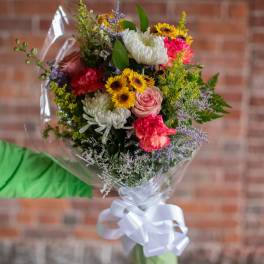 Mixed bouquet of colorful flowers wrapped in clear plastic with a white ribbon