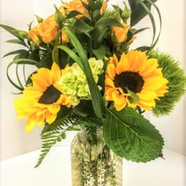 Sunflowers and orange roses arranged in a clear glass vase