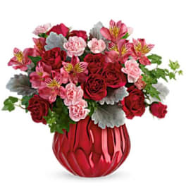 Red roses and pink flowers in a red glass vase