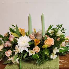 Low floral centerpiece with roses, lilies, and two green candles