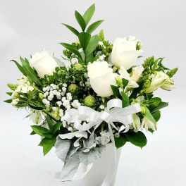 White roses and mixed white flowers in a white vase with a ribbon