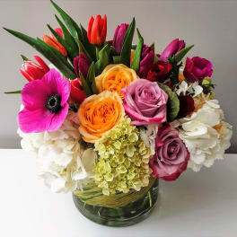 Colorful bouquet of roses, tulips, anemone, and hydrangea in a glass vase