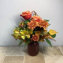 Orange roses and yellow flowers in a brown textured vase