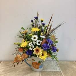 Mixed yellow, white, and purple flowers in a pumpkin mug