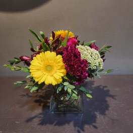 Mixed bouquet in a square glass vase with yellow daisies and magenta blooms