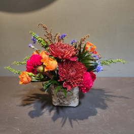 Mixed bouquet of orange roses, red chrysanthemums, and pink carnations in a square vase