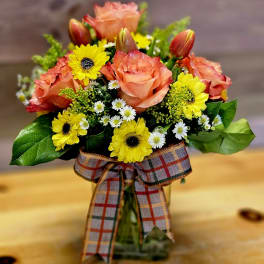 Bouquet of peach roses and yellow daisies in a glass vase with a plaid ribbon