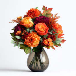 Orange and burgundy flowers arranged in a smoky glass vase