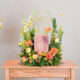 Floral arrangement with orange gerbera daisies and roses around a pink urn.