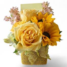 Yellow roses and sunflowers in a woven basket with pale pink flowers