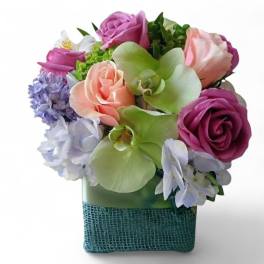 Mixed bouquet of roses, orchids, and hydrangeas in a square vase