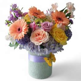 Mixed bouquet in a wrapped cylindrical vase with peach, purple, and yellow flowers