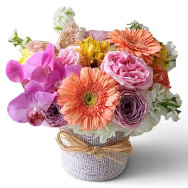 Mixed bouquet in a burlap-wrapped vase with pink, peach, purple, and white flowers