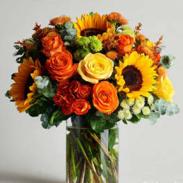 Bouquet of sunflowers and orange roses in a clear glass vase