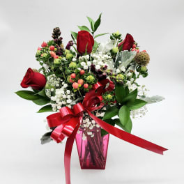 Red roses and mixed white flowers in a pink vase with a red ribbon