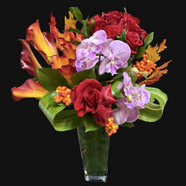 Bouquet of red roses, purple orchids, and orange calla lilies in a glass vase
