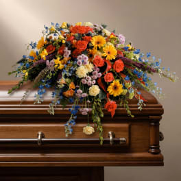 Colorful floral casket spray with roses, daisies, and trailing blooms