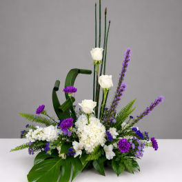 Tall floral arrangement with white roses, purple flowers, and tropical leaves