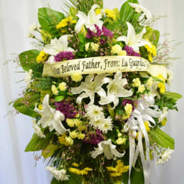Large funeral spray with white lilies, yellow and purple flowers, and a memorial ribbon