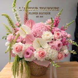 Pink and white floral arrangement in a wicker basket with ribbon