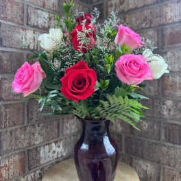 Pink, red, and white roses arranged in a dark glass vase