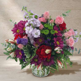 Mixed bouquet of pink, purple, red, and white flowers in a clear glass vase