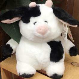 Plush black-and-white cow toy sitting on a wooden shelf