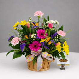 Mixed bouquet in a wooden basket with pink, yellow, purple, and white flowers