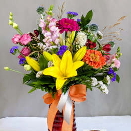 Colorful mixed bouquet in a red glass vase with an orange ribbon