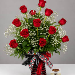 Red roses arranged in a red glass vase with white filler flowers