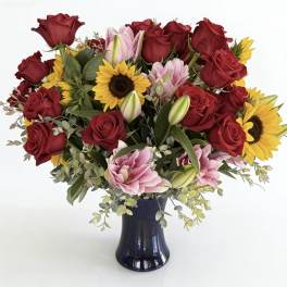 Bouquet of red roses, pink lilies, and sunflowers in a dark vase
