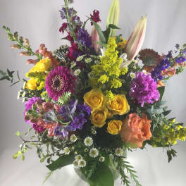 Mixed bouquet with yellow roses, lilies, and purple flowers in a glass vase
