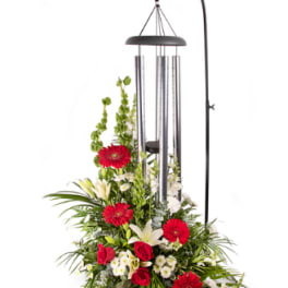 Standing floral arrangement with red gerberas, roses, and white lilies under a wind chime