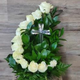 White roses arranged around a clear cross with green foliage