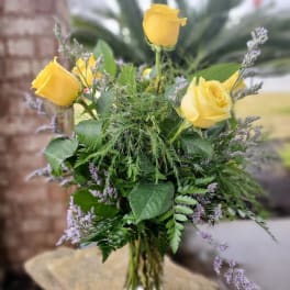 Yellow roses in a clear glass vase with mixed greenery