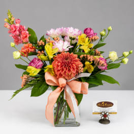 Colorful mixed bouquet in a clear glass vase with a peach ribbon