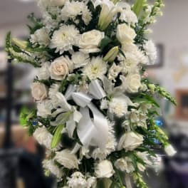 Tall white standing spray with roses, lilies, mums, and snapdragons on a stand with a white bow.