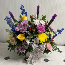 Colorful mixed flower arrangement in a white basket with a floral ribbon