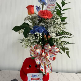 Tall mixed flower arrangement with a plush teacher bear and gift sign in a glass vase
