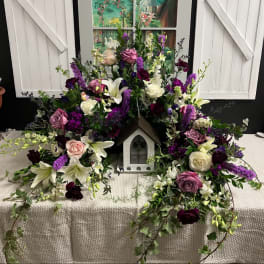 Floral wreath around a small decorative house with white and purple flowers