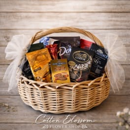 Wicker gift basket filled with assorted boxed and bagged chocolates, tied with sheer white ribbon bows.
