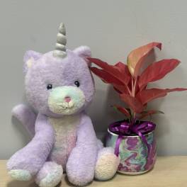 Plush unicorn beside a potted red-leaf plant in a decorative can
