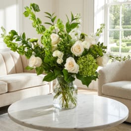 White roses and green flowers in a clear glass vase