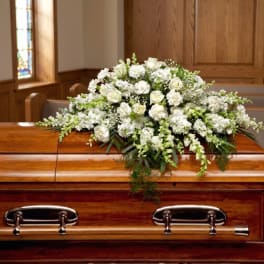 White floral casket spray with roses and carnations on a wooden casket