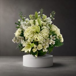 White floral arrangement with lilies, roses, and hydrangeas in a low vase